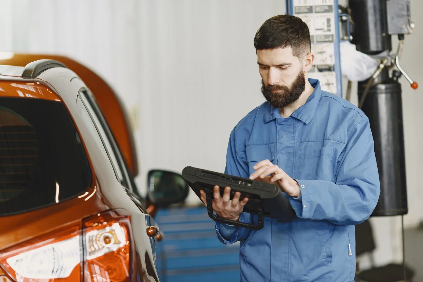 Mechaniker mit Diagnosegerät neben einem Fahrzeug in einer Werkstatt, illustratives Stockfoto
